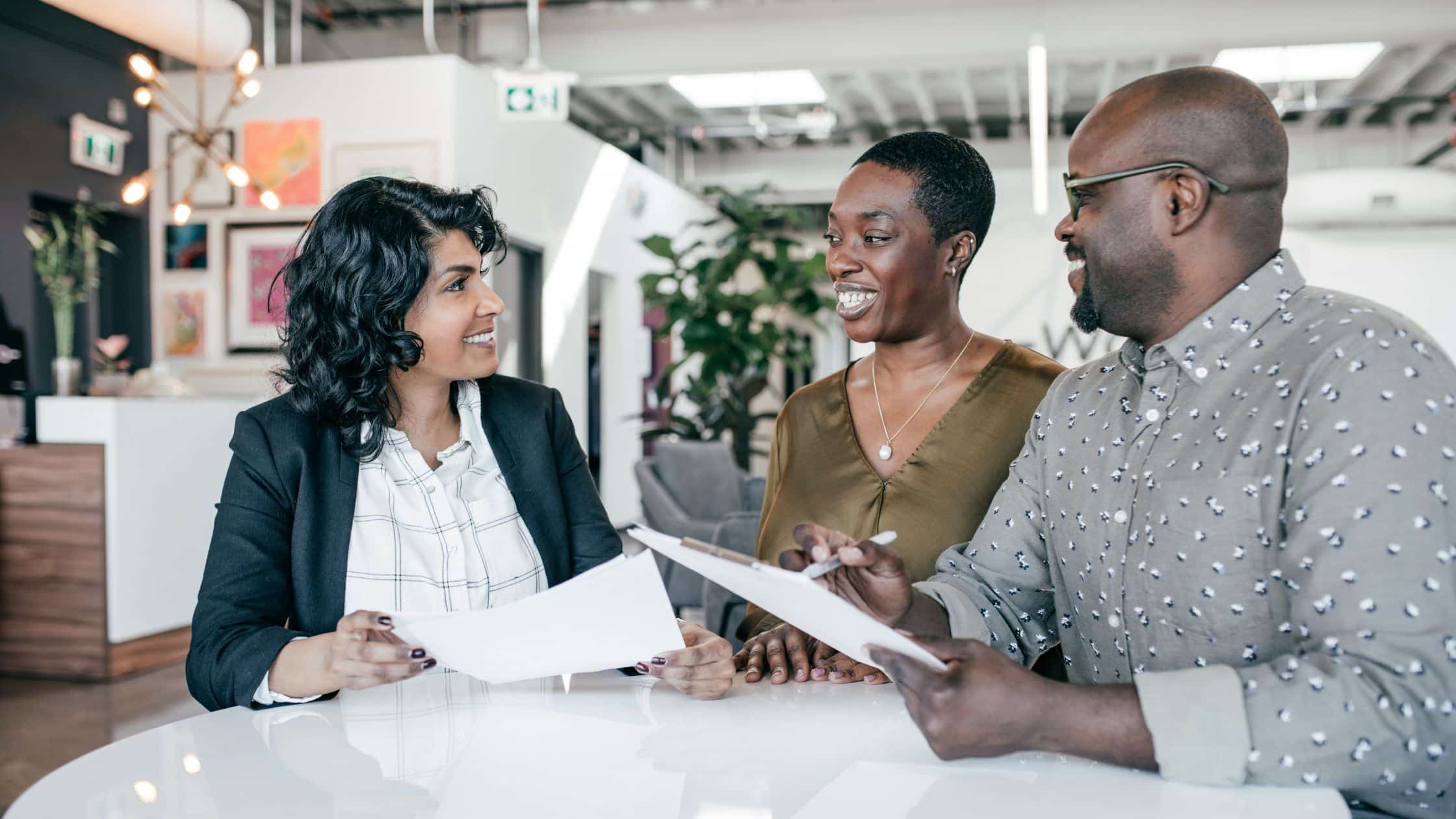A lawyer for estate planning discusses documents with a smiling couple in a modern office setting.