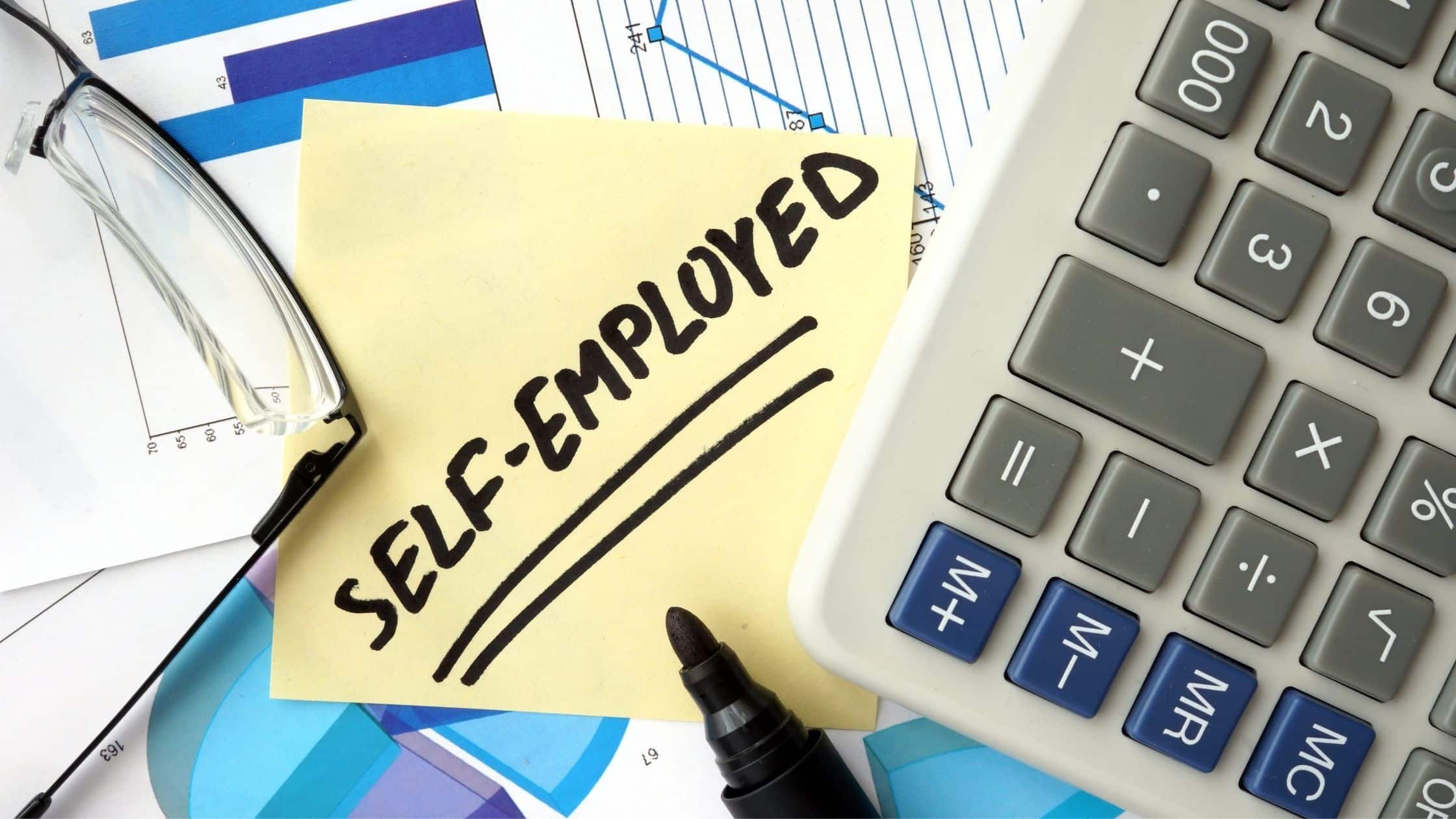 elf employed tax deductions concept shown with sticky note reading 'self-employed', calculator, glasses, and financial charts.